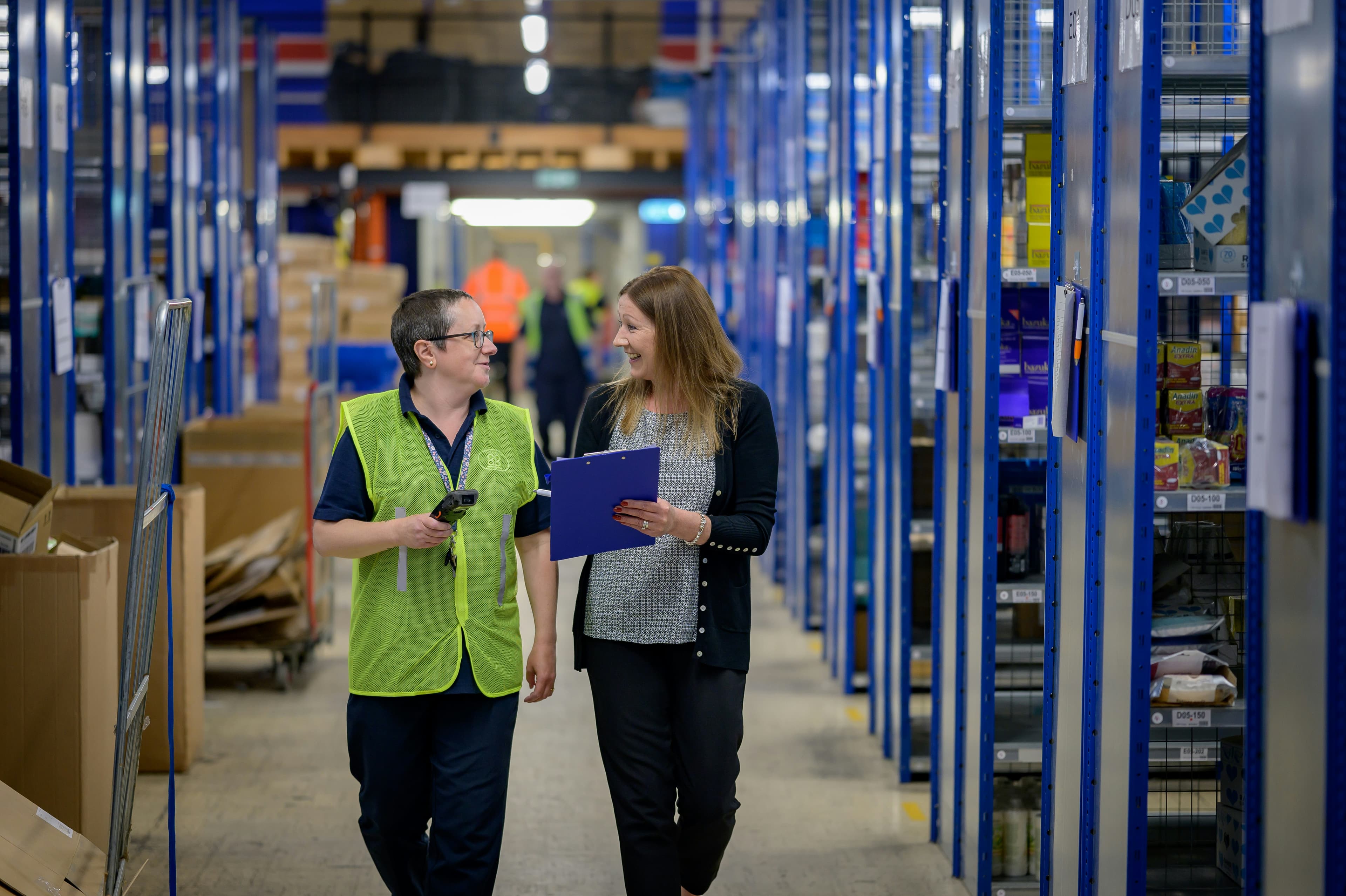 Two people walking through a warehouse and chatting.